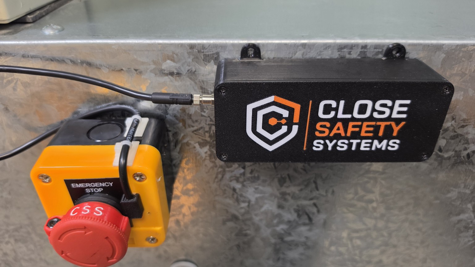 Close view of the CSS field unit and retrofit sensor beside an emergency stop